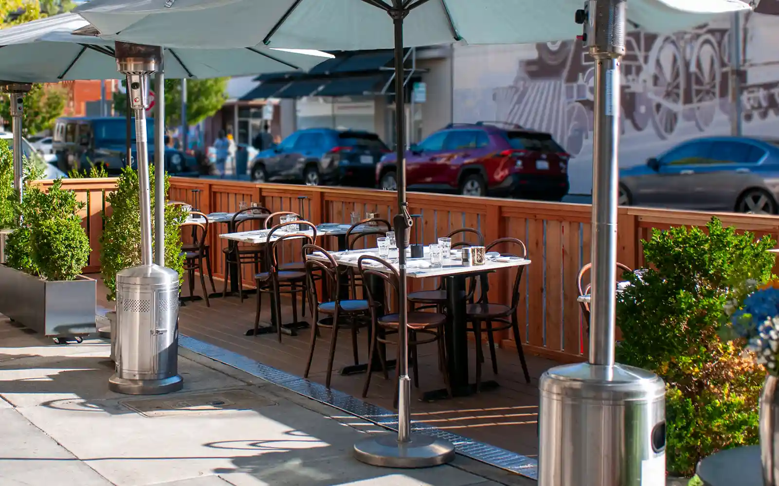 Bistro Elan's parklet facing Birch St. Enjoy outdoor dining near California Avenue in Palo Alto. Tables and chairs are set up for your comfort, with lush greenery in the background.