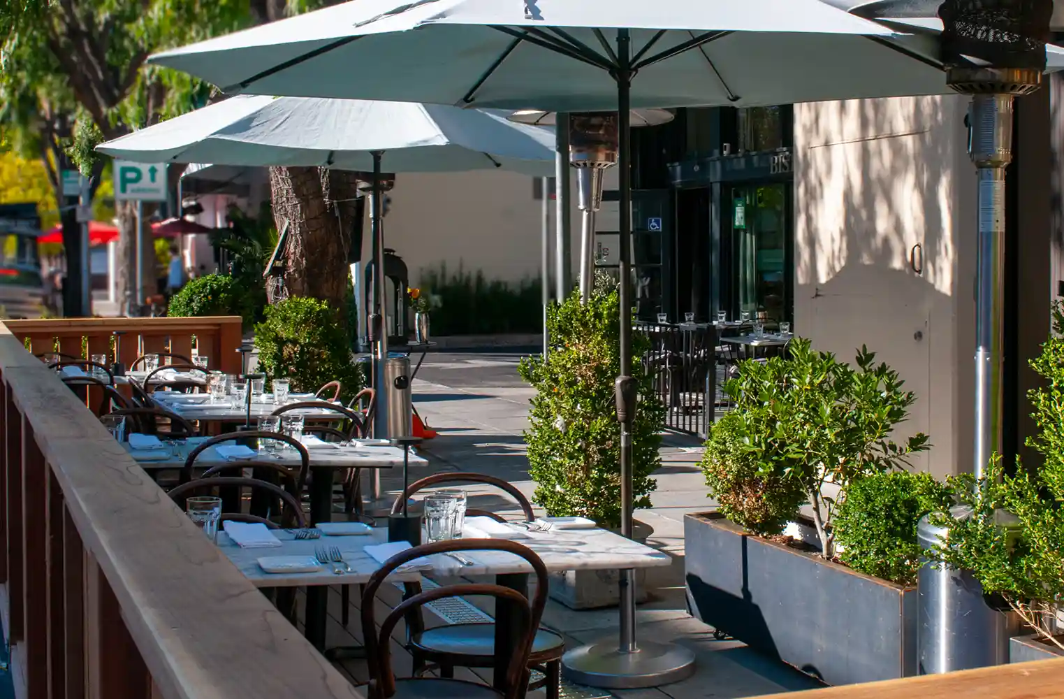 Tables al fresco at Bistro Elan's parklet, vibrant plants and trees enhancing the charming Silicon Valley atmosphere.