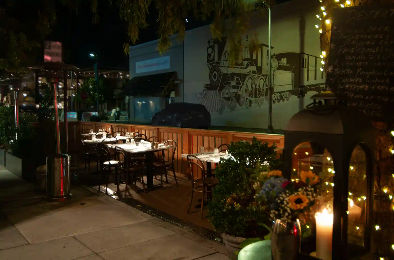 A nighttime view of Bistro Elan's parklet dining area, featuring elegantly arranged tables and a welcoming ambiance, perfect for a meal near California Avenue.