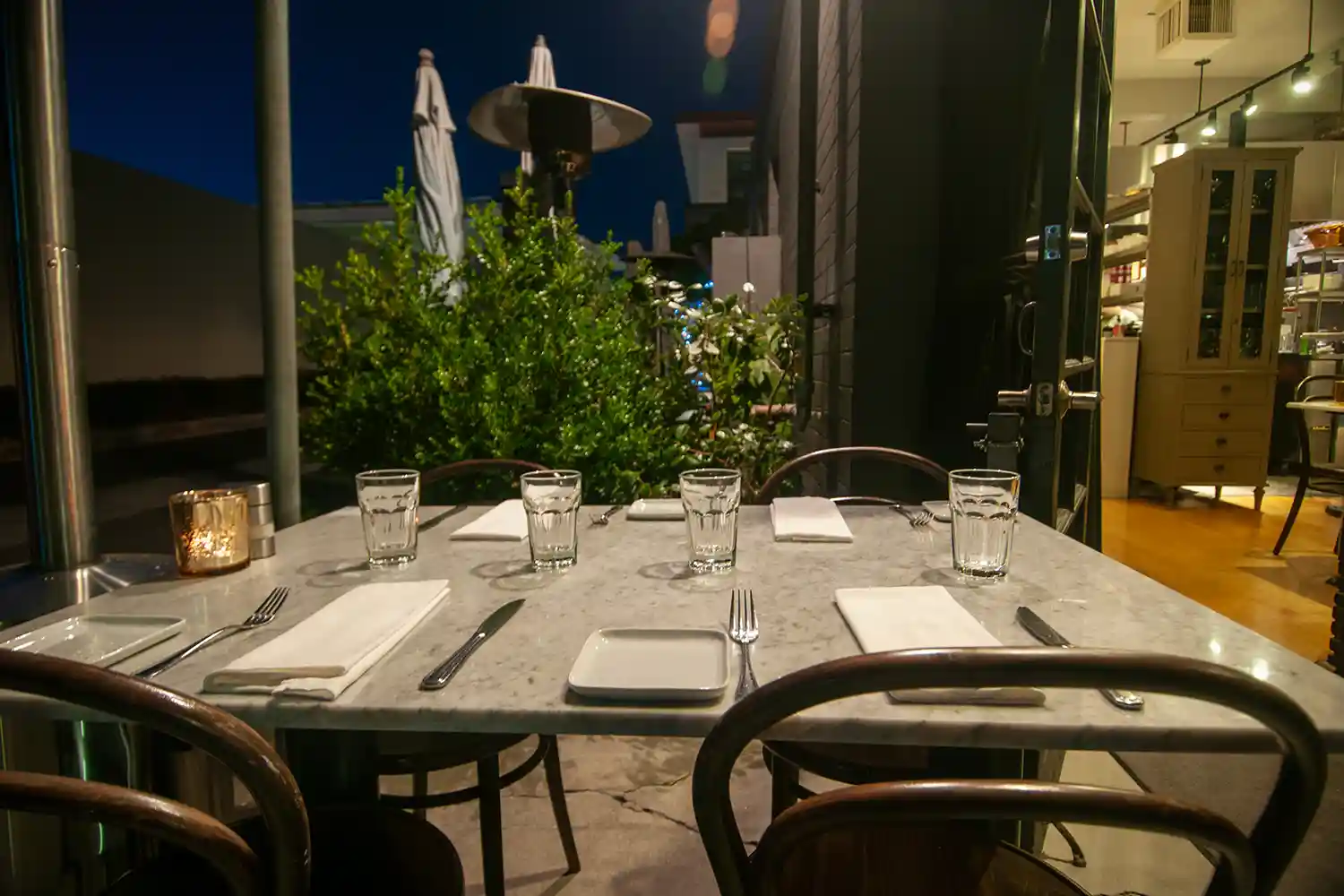 View of the charming patio at Bistro Elan, with stylish tables set under leafy trees, inviting diners to enjoy the California sun in Palo Alto.